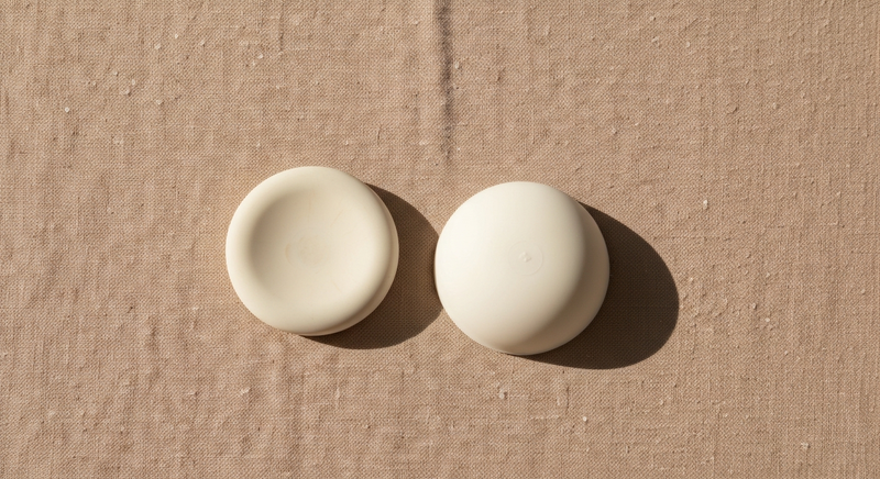 Flatlay of neutral linen fabric with small smooth silicone disc in soft morning light, minimal editorial