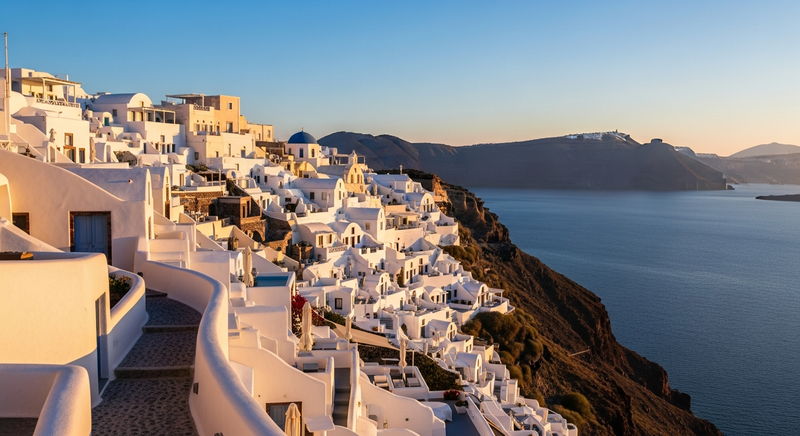 Late afternoon light on whitewashed caldera walls in Oia, Santorini, blue dome visible, volcanic cliffs descending to the sea